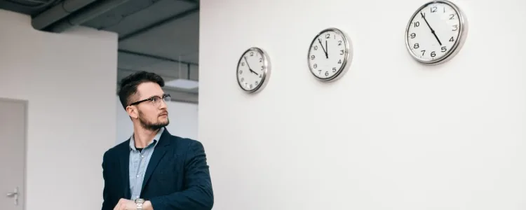 Hombre mirando su reloj junto a una pared de relojes, símbolo de la nueva ley de control horario Hombre mirando su reloj junto a una pared de relojes, símbolo de la nueva ley de control horario